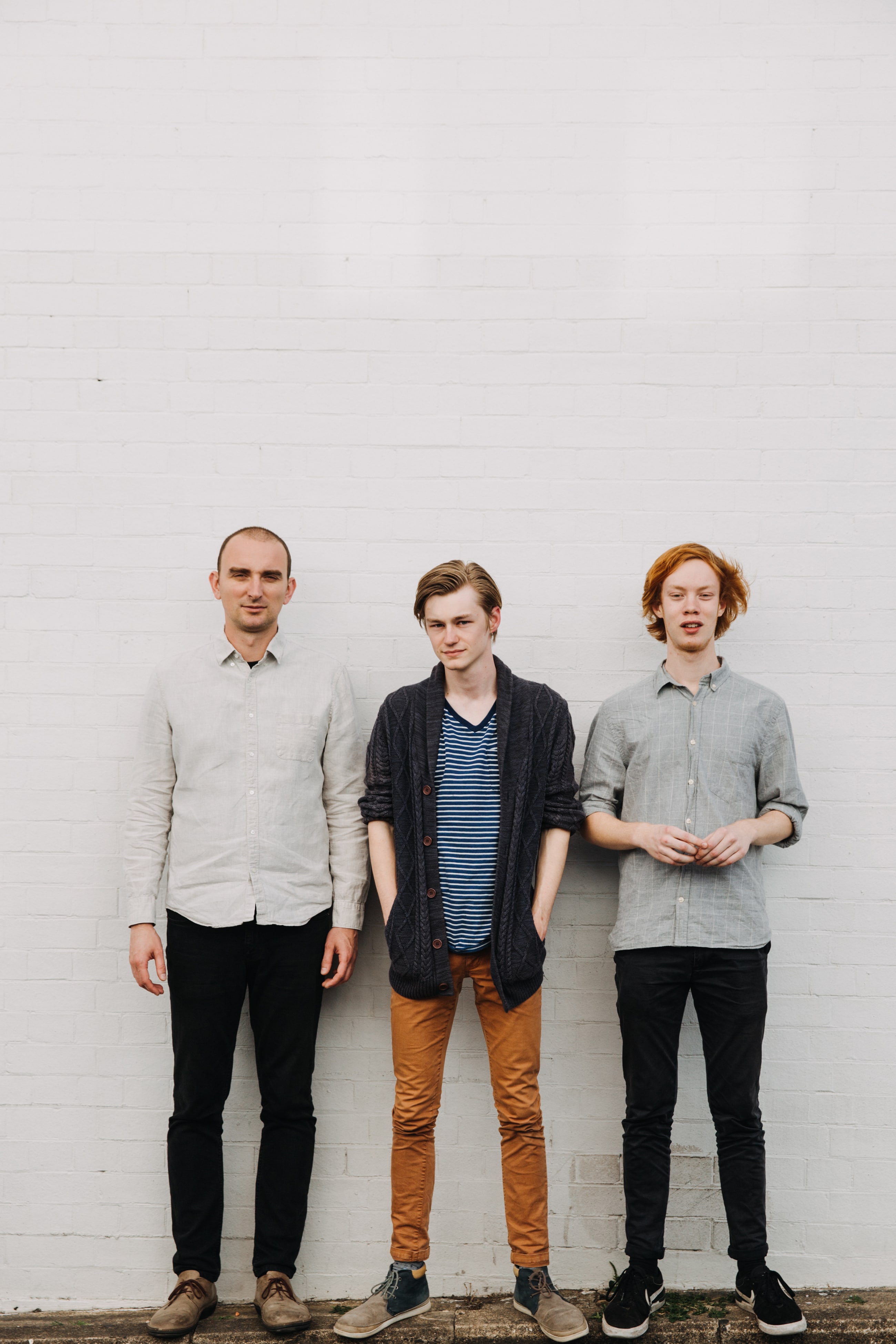 The Sam Hewerdine Trio, standing in front of a white wall 